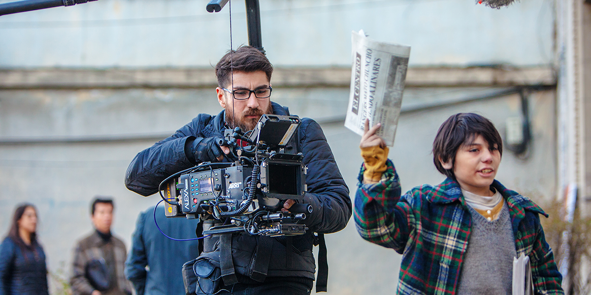 Photo of Andres Gallegos filming a boy holding up a newspaper